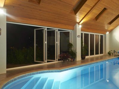 smarts visofold 1000 doors opening up a swimming pool area into a garden at night time